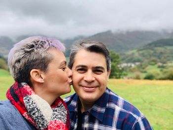 Woman kissing on man cheek against sky