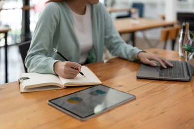 Midsection of woman using mobile phone at table