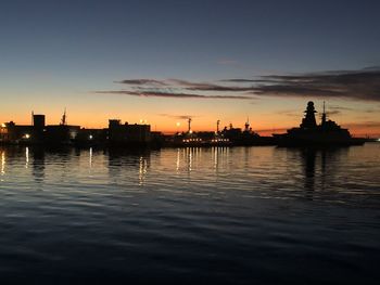 Silhouette buildings by sea against sky during sunset