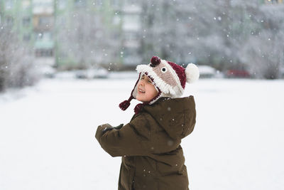 Cute little boy in funny winter hat walks during a snowfall. outdoors winter activities for kids.