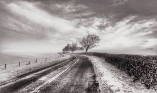 Dirt road amidst field against sky