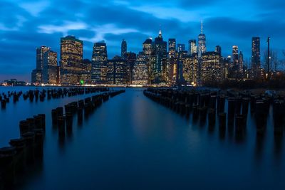 Illuminated city at waterfront against cloudy sky