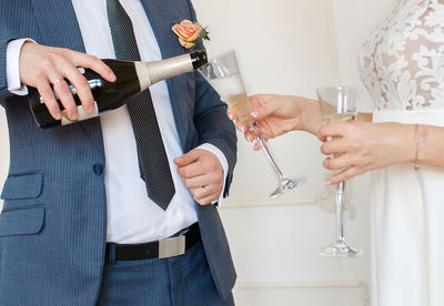 Midsection of groom pouring champagne in bride flute during wedding 