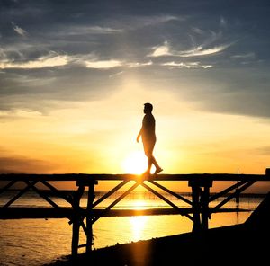 Silhouette man standing by sea against sky during sunset