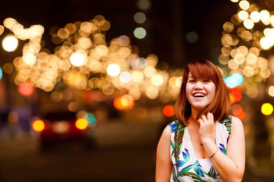 Portrait of happy woman in city against illuminated street light