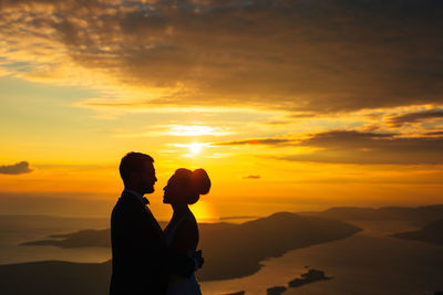 Silhouette friends standing against orange sky