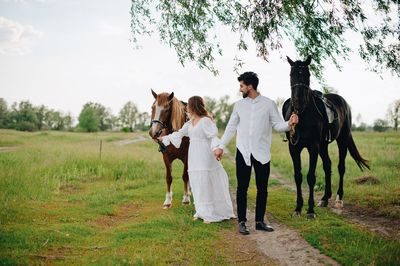 Couple standing by horses on field