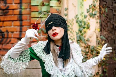 Portrait of young woman in halloween costume and mask standing outdoors by brick wall in autumn