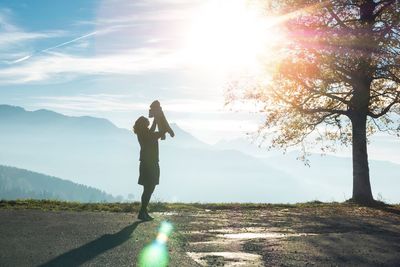 Woman with baby standing on road against sky during sunset