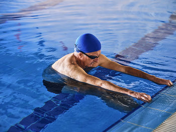 Mature man in swimming cap standing in pool during water aerobics class