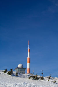 Tower on snow covered land against clear blue sky