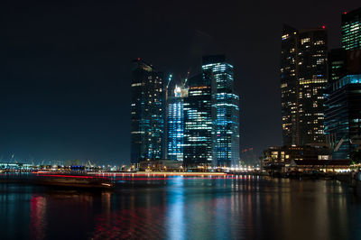 Illuminated buildings by river against sky at night