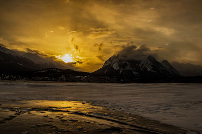 Scenic view of frozen lake against dramatic sky during sunset