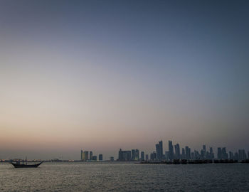 Sea by buildings against clear sky during sunset