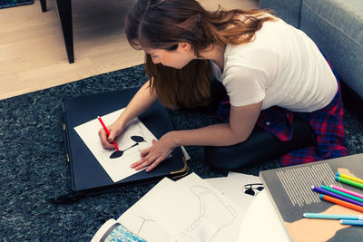 Side view of woman sitting with drawings at home