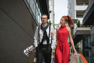 Couple holding shopping bags while walking amidst buildings in city