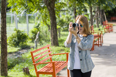 Young woman photographing through mobile phone while standing in park