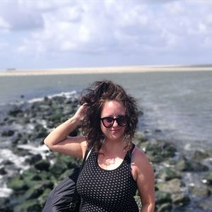 Young woman wearing sunglasses standing at beach against sky