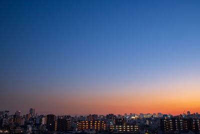 Illuminated buildings against clear blue sky during sunset