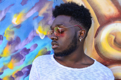 Young man wearing sunglasses looking away standing against multi colored wall