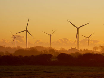 Windmills on field against sky during sunset