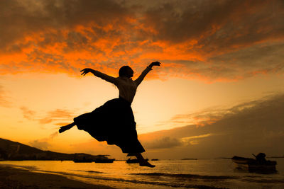 Silhouette of woman jumping in sea at sunset