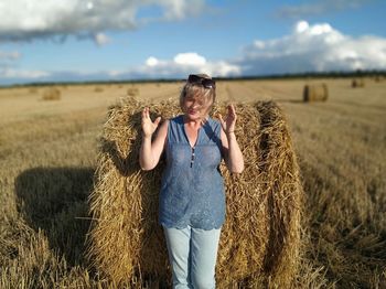 Midsection of woman with hay bales on field against sky