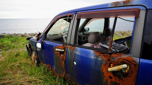 Abandoned car on field by sea against sky