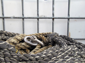 Close-up of ropes with hook by railing against wall