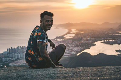 Portrait of man sitting on rock above cityscape