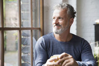 Mture man taking a break, drinking coffee at the window of his loft apartment