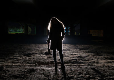 Silhouette young woman holding axe while standing indoors at night