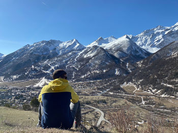 Rear view of man sitting on snowcapped mountain against sky