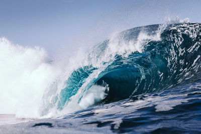 Sea waves splashing on beach against sky