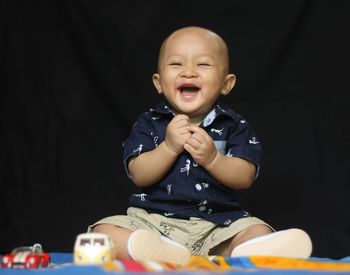 Portrait of cute baby boy sitting against black background