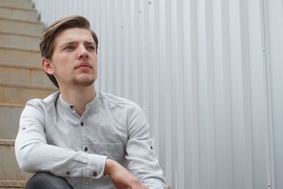 Thoughtful young man looking away while sitting on steps