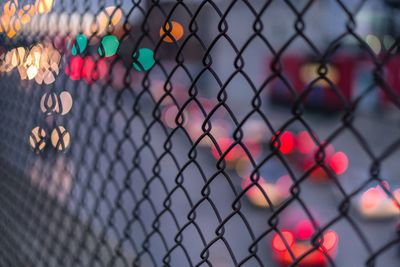 Full frame shot of chainlink fence in illuminated city during dusk