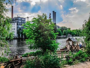 Bridge over river amidst trees and buildings against sky