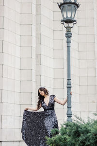 Beautiful woman holding street light while posing against wall