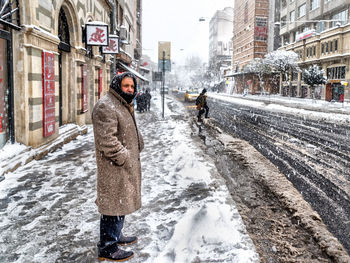 Man standing on snow covered street in city