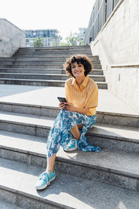 Smiling woman with smart phone sitting on steps