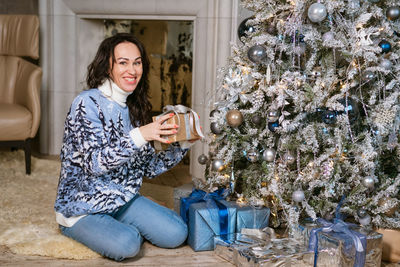 Smiling caucasian woman opens box of christmas present in knitted sweater