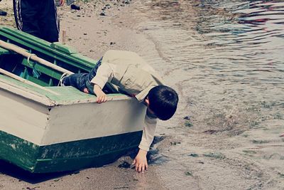 High angle view of boy bending on boat moored at riverbank