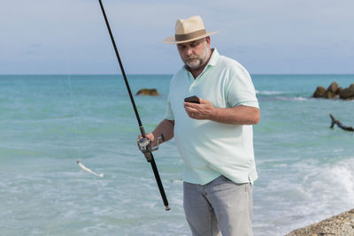 Focused mature man with a fishing rod and a phone