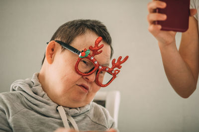 Sleepy elderly woman with down syndrome in funny christmas glasses, video call from phone