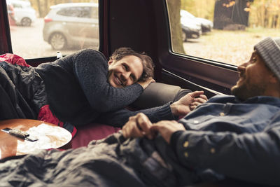 Happy man talking with male friend while lying in motor home during vacation