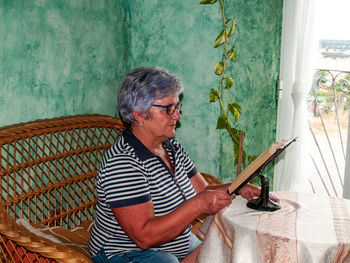 Woman reading book while sitting by window at home