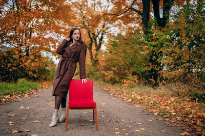 Young beautiful woman with old armchair on the country lane in autumn