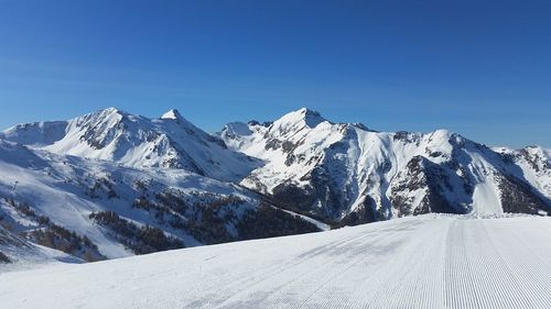 Snow covered landscape against clear blue sky