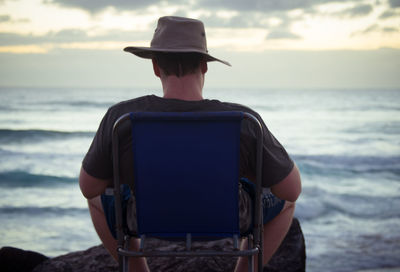 Rear view of man sitting on chair at beach during sunset